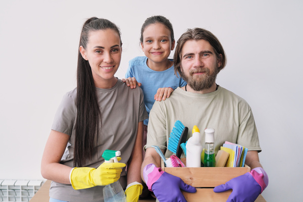 Photo of a young family in colorful rubber gloves with a cleaning set and a sprayer filled with cleaning agent in their hands